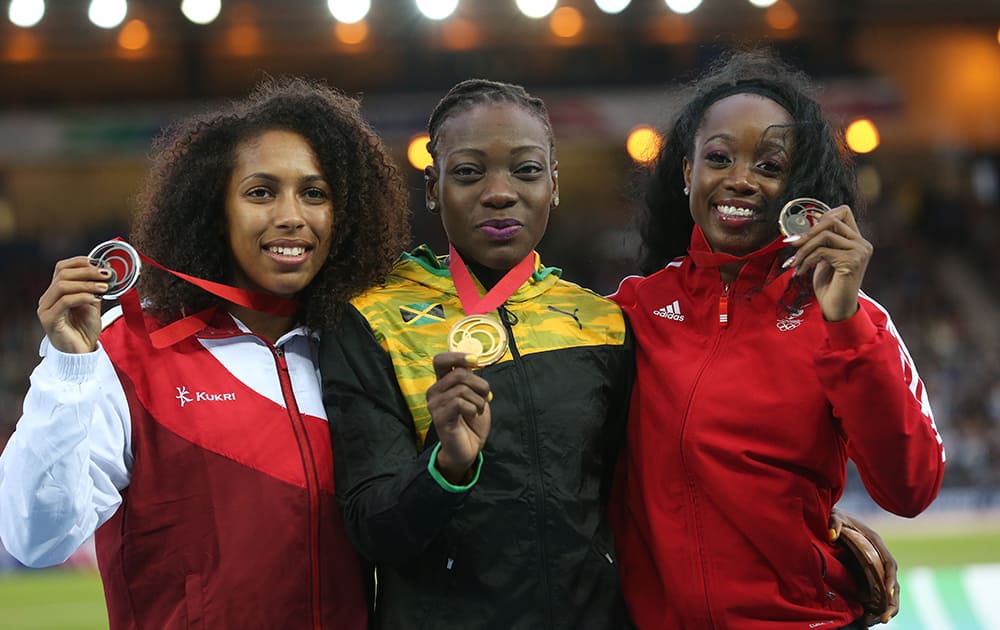 Kimberly Williams, holds up her gold medal for winning the women's triple jump, with Laura Samuel, who won the silver medal and Ayanna Alexander of Trinidad and Tobago who won the bronze medal as they pose for photographs following the medal ceremony for the event in Hampden Park stadium.