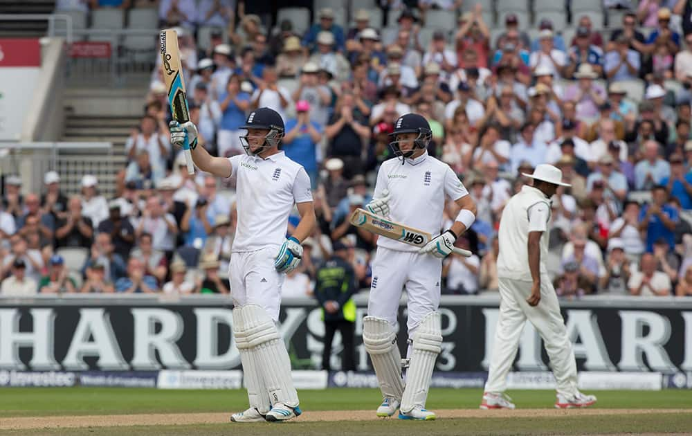 As teammate Joe Root looks on England's Jos Buttler raises his bat as he reaches 50 on the third day of the fourth test match of their five match series against India at Old Trafford cricket ground, in Manchester, England.