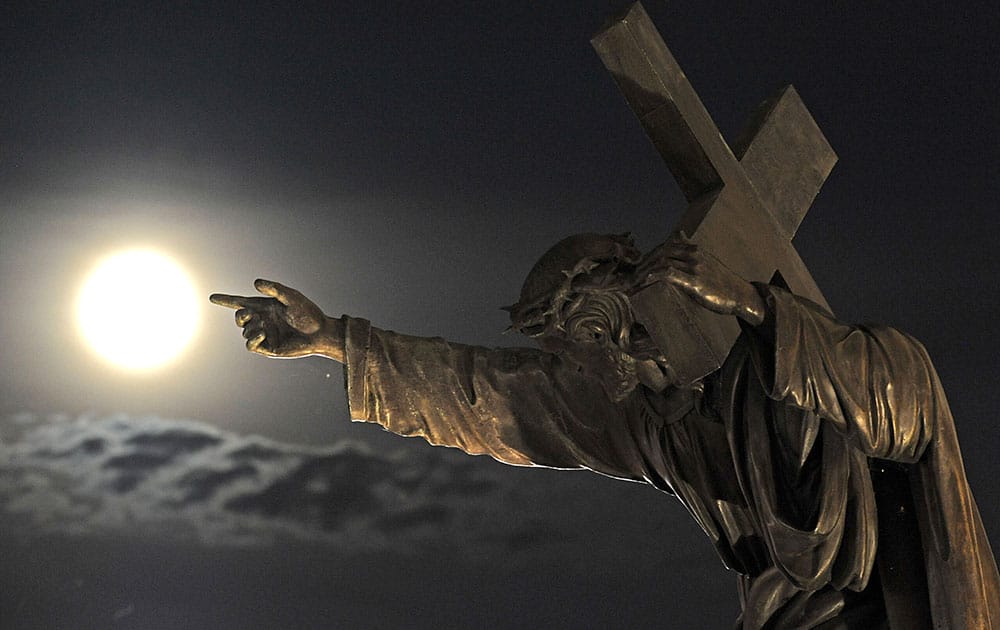 A SUPERMOON RISES ABOVE A JESUS CHRIST STATUE IN FRONT OF THE HOLY CROSS CHURCH IN WARSAW, POLAND.