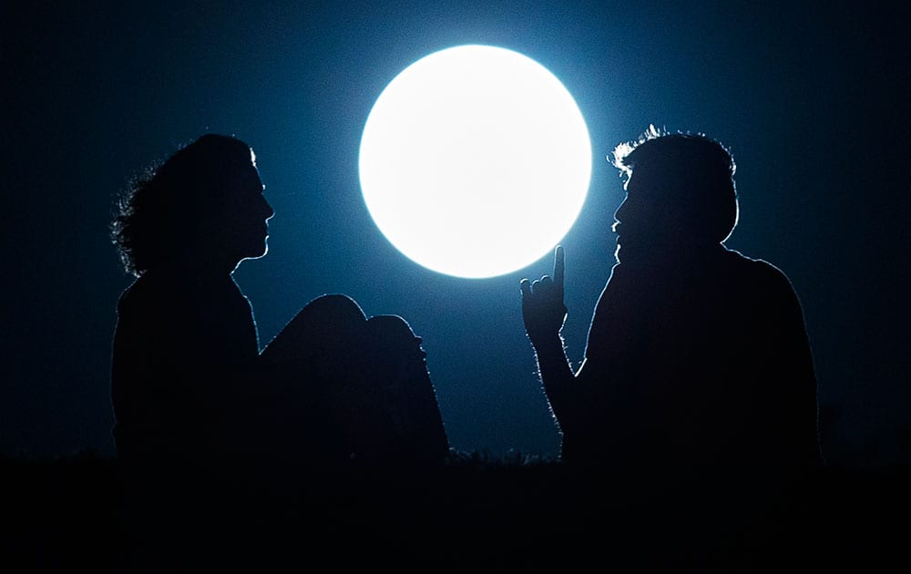 A couple talk as they sit against the perigee moon, also known as a supermoon, in Madrid.