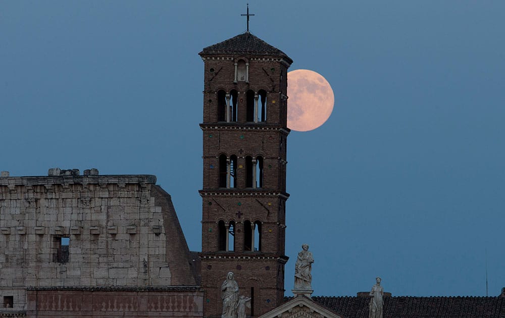 The moon appears above the Colosseum and the ancient Santa Francesca Romana Basilica belltower, in Rome.