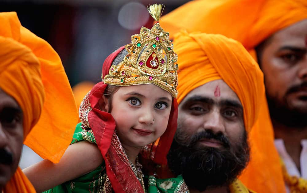 An Indian man carries a girl dressed as Radha, consort of Hindu god Krishna, during a procession on the eve of Janmashthami festival in Jammu.