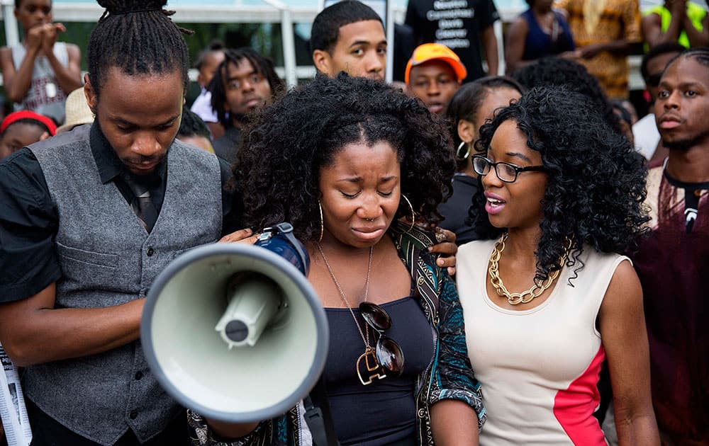 Elle Lucier, center, is comforted by Shawn Walton, left, and Sheola Farquharson as she pauses while fighting back tears during a speech at a rally in response to the fatal shooting of Michael Brown,  in Atlanta. 