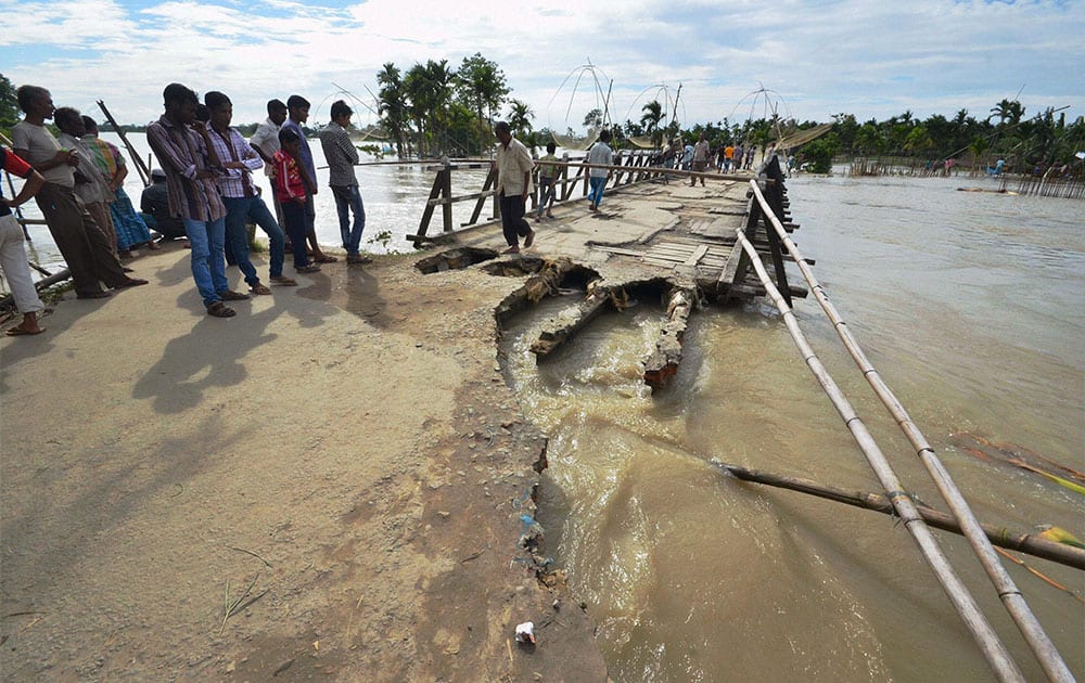 Villagers stand near a damaged bridge on flooded Brahmaputra river at Lawkhowa village in Nagaon district of Assam.