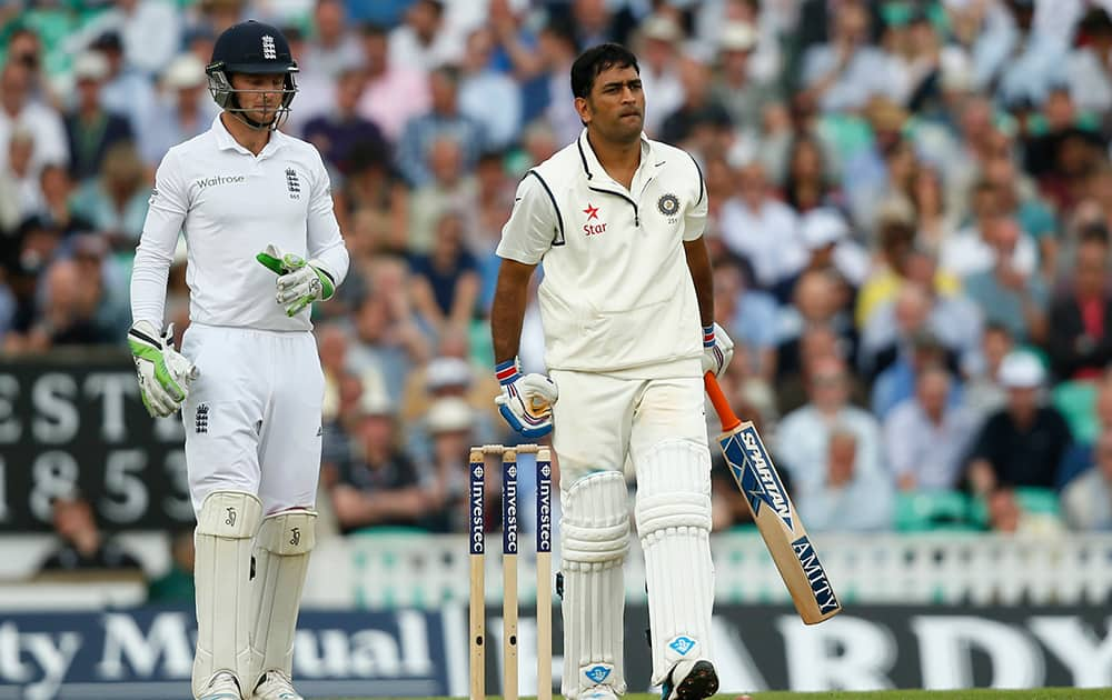 England's wicketkeeper Jos Buttler walks to collect the ball after India's MS Dhoni, right, played a shot during the first day of the fifth Test cricket match at Oval cricket ground in London.