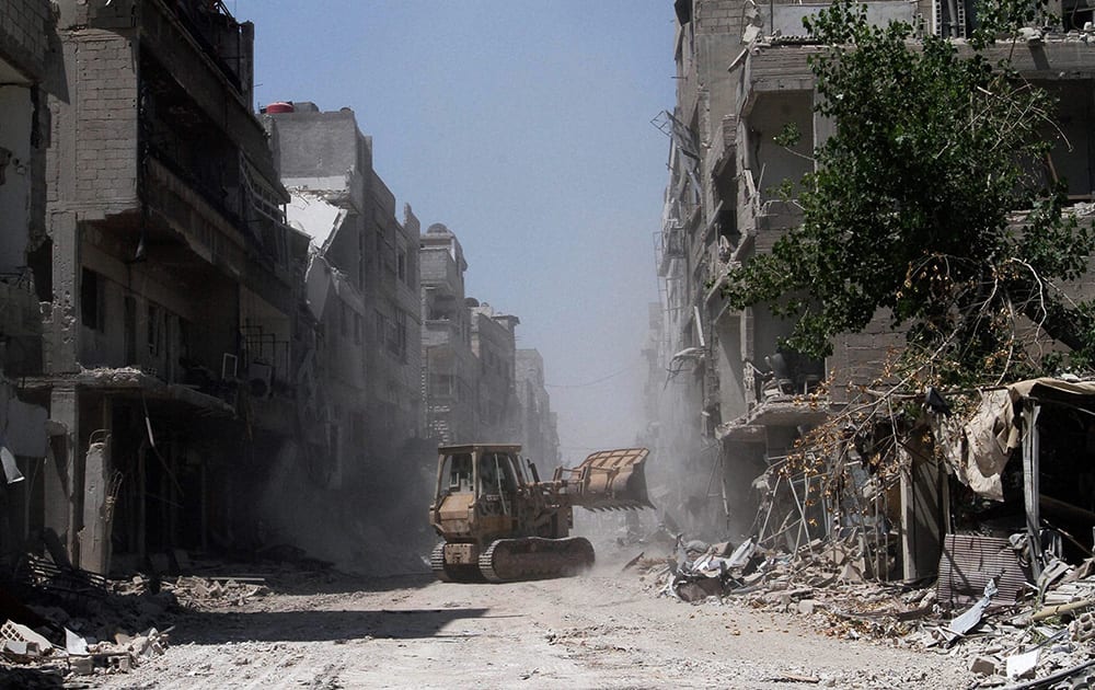 This photo taken during a Syrian government-led media tour, a man operates a bulldozer to clear debris created during battles between Syrian troops and rebels off a street in Mleiha, some 10 kilometers (6 miles) southeast of downtown Damascus, Syria.