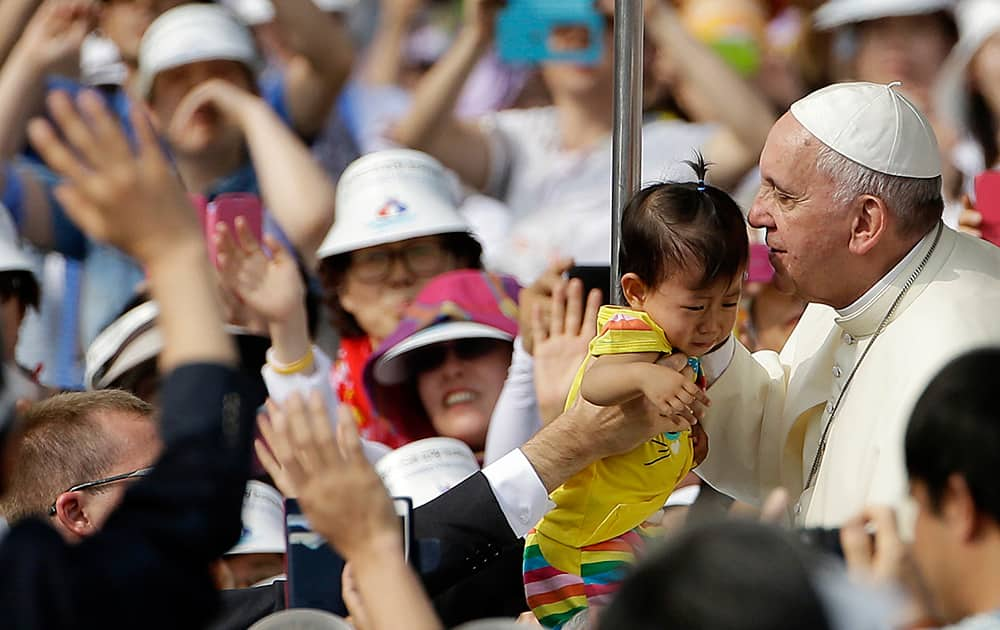 Pope Francis kisses a baby as he arrives with the popemobile to celebrate a mass and the beatification Paul Yun ji-Chung and 123 martyr companions at Gwanghwamun Gate in Seoul, South Korea.