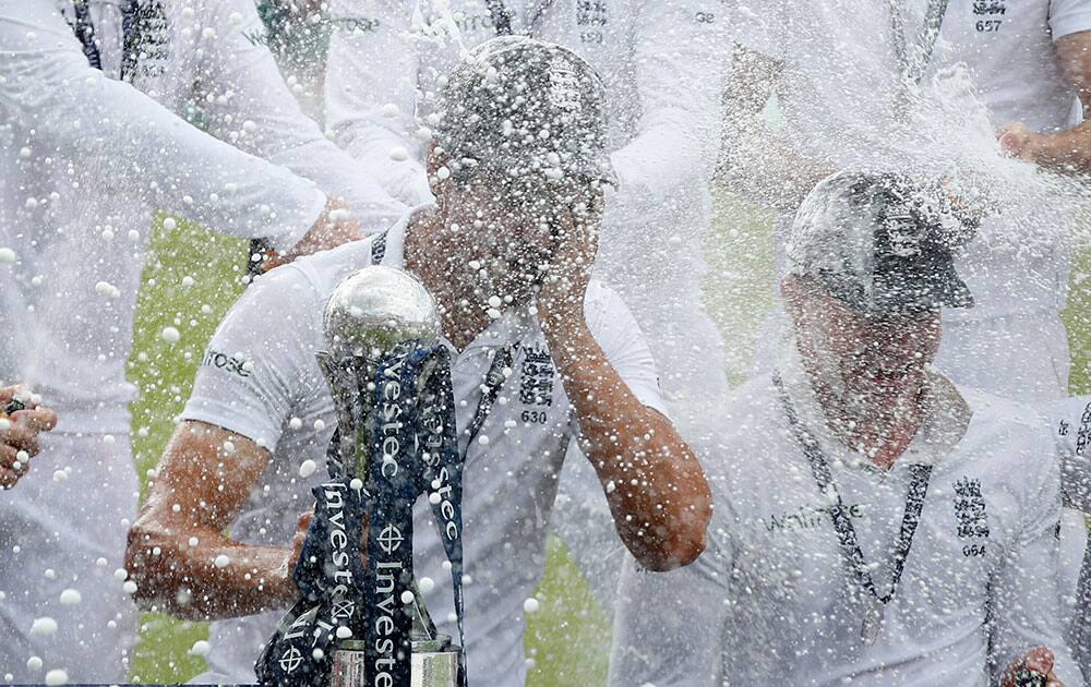 England cricket team captain Alastair Cook holds the trophy as the team celebrate with champagne their 3-1 series win, after defeating India on the third day of the fifth test cricket match at Oval cricket ground in London.