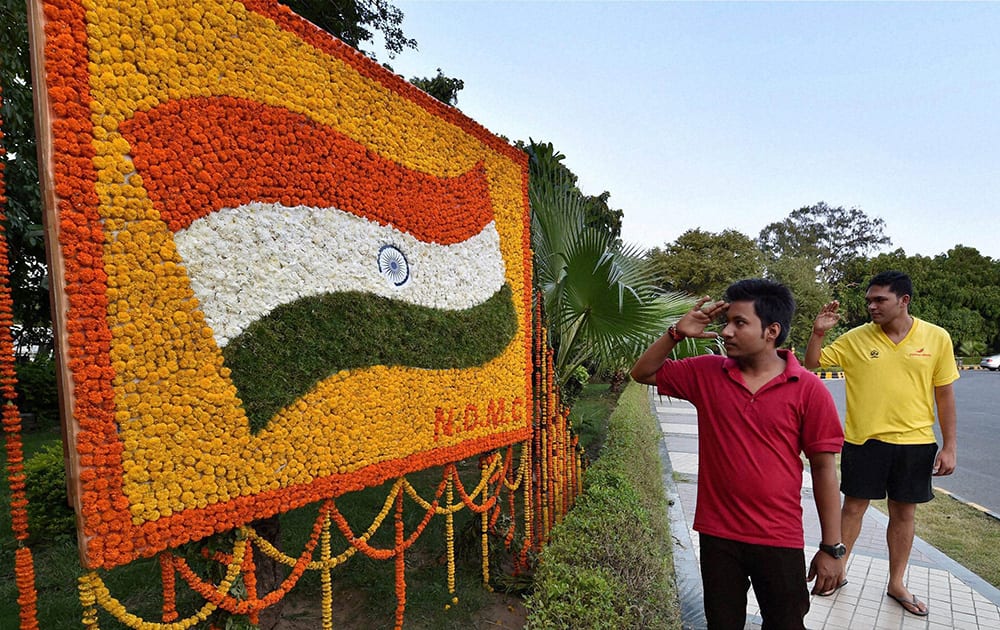 Two youth salute a Tricolor made with flowers on a display board at a pavement in New Delhi on the eve of Independence Day.