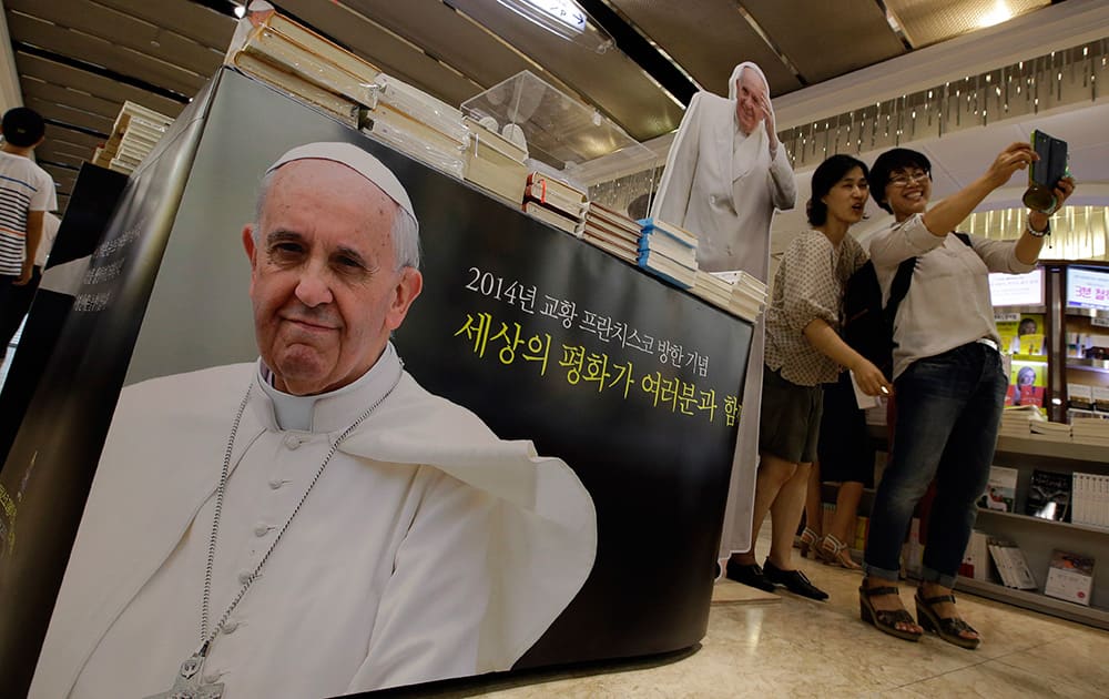 Visitors take their souvenir photos near pictures of Pope Francis at a bookstore in Seoul, South Korea. Pope Francis is scheduled to make a five-day trip to South Korea.