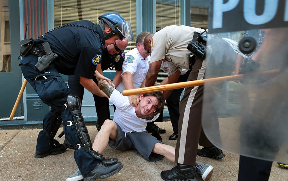 Police officers arrest a man who refused to leave when police in riot gear cleared the area of S. Florissant Road and Church Street in downtown Ferguson, Mo.