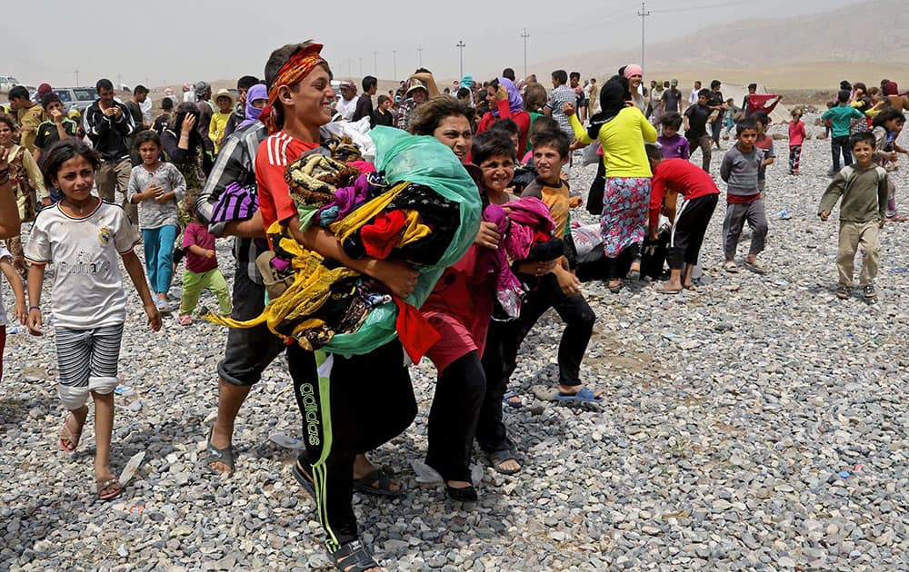 Displaced Iraqis carry clothes provided by a charity as they settle at a new camp outside the Bajid Kandala camp in Feeshkhabour town, Iraq.