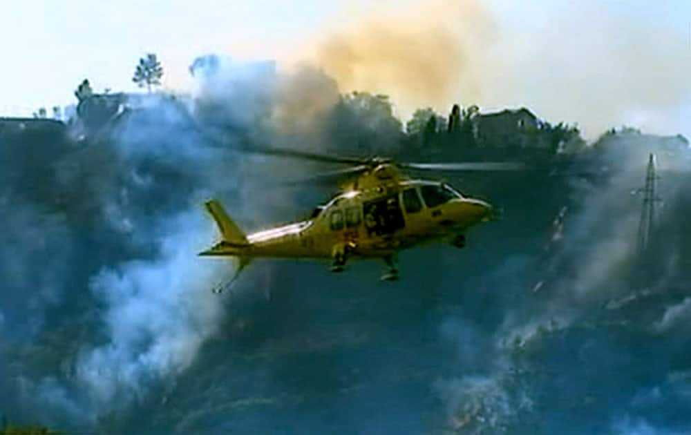 In this frame grab from a footage by Rainews 24, a rescue helicopter overflies the flames burning the bush after two Italian air force fighter jets carrying a total of four crew members collided during a training mission over Italy and crashed into a hilly, wooded area that erupted in flames, Tuesday, near Venarotta some 20 kilometers from Ascoli Piceno, Central Italy.