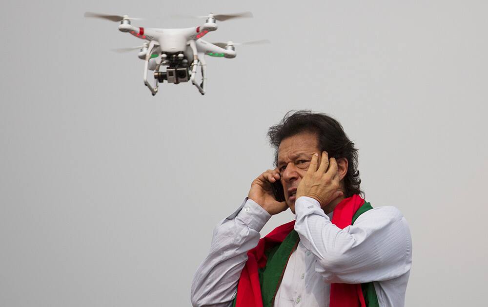 Pakistan`s cricketer-turned-politician Imran Khan talks over a phone as a camera-equipped drone hovers outside a parliament in Islamabad, Pakistan.