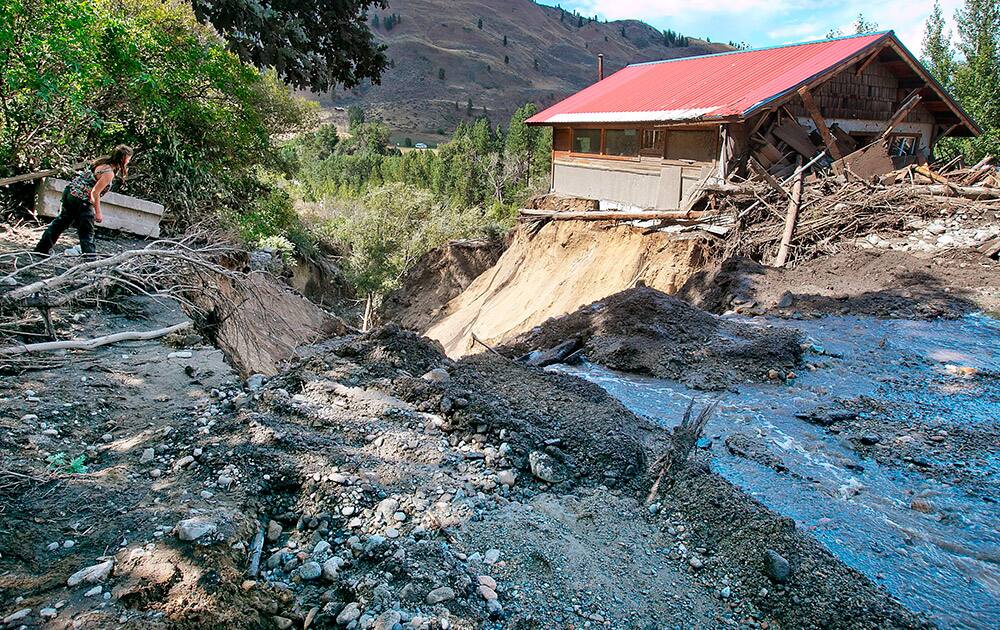 A neighbor tries to get a closer look, at a canyon that was gouged out during a flood the previous night alongside Highway 153 a mile north of Carlton, Wash. Mud and debris washed onto roadways when heavy rain fell on land scarred by wildfires in north central Washington.