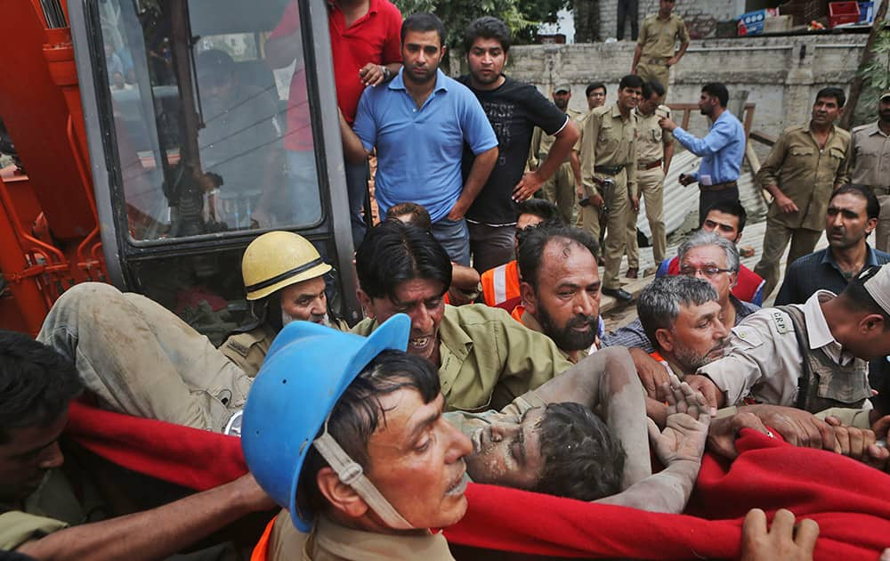 Rescue workers carry an injured laborer out of the debris of a building that collapsed in Srinagar.