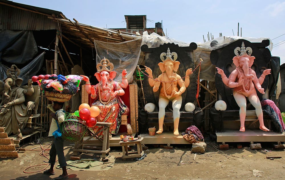 A vendor carries plastic goods and walks past idols of Hindu god Ganesha kept on display for sale ahead of Ganesha Chaturthi festival in Guwahati.