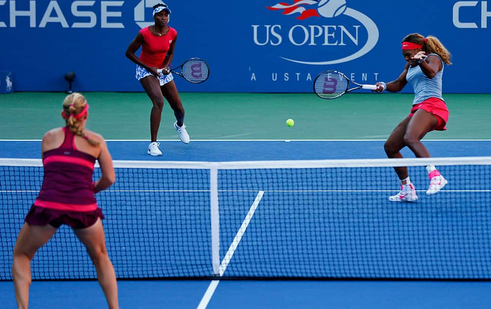 Serena Williams, right, returns a shot as Venus Williams, center, looks on during a doubles match against Timea Babos and Kristina Mladenovic during the 2014 US Open tennis tournament in New York.