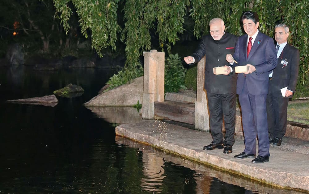 Prime Minister Narendra Modi, left, and his Japanese counterpart Shinzo Abe, center, feed carp in a pond at the State Guest House in Kyoto, western Japan.