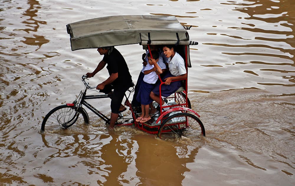 School children sit on a Rickshaw on their way through a flooded street in Guwahati.