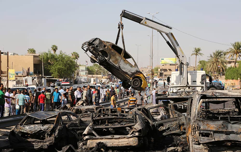 People and security forces gather as a destroyed car is moved from the site of a car bomb explosion in southeastern neighborhood of New Baghdad, Iraq.