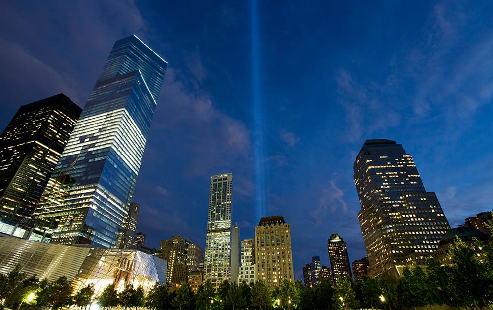 The Tribute in Light rises behind buildings adjacent to the World Trade Center in New York. The art installation consists of 88 searchlights aiming skyward in two columns, in memory of the former twin towers. Four World Trade Center is at left.
