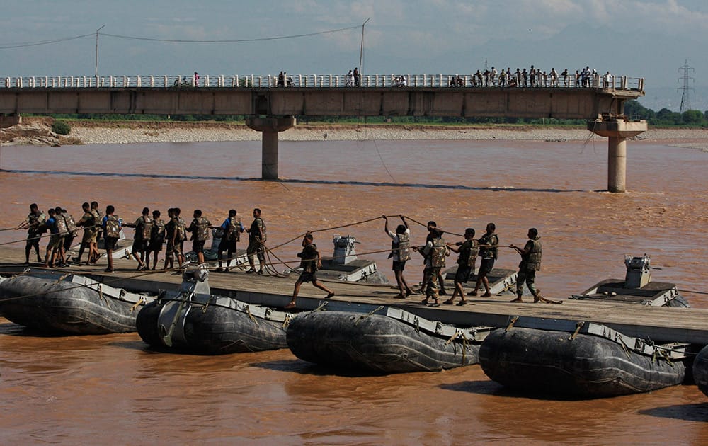 Indian army soldiers build a temporary bridge across the Tawi River after the existing bridge was damaged in the floods on the outskirts of Jammu.