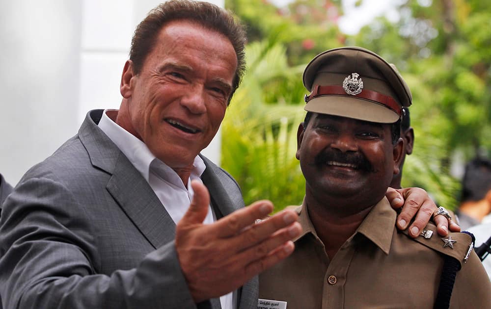 Hollywood star Arnold Schwarzenegger poses with an Indian police officer and gestures to the waiting media as he returns after visiting Tamil Nadu state Chief Minister Jayaram Jayalalitha at her office in Chennai.