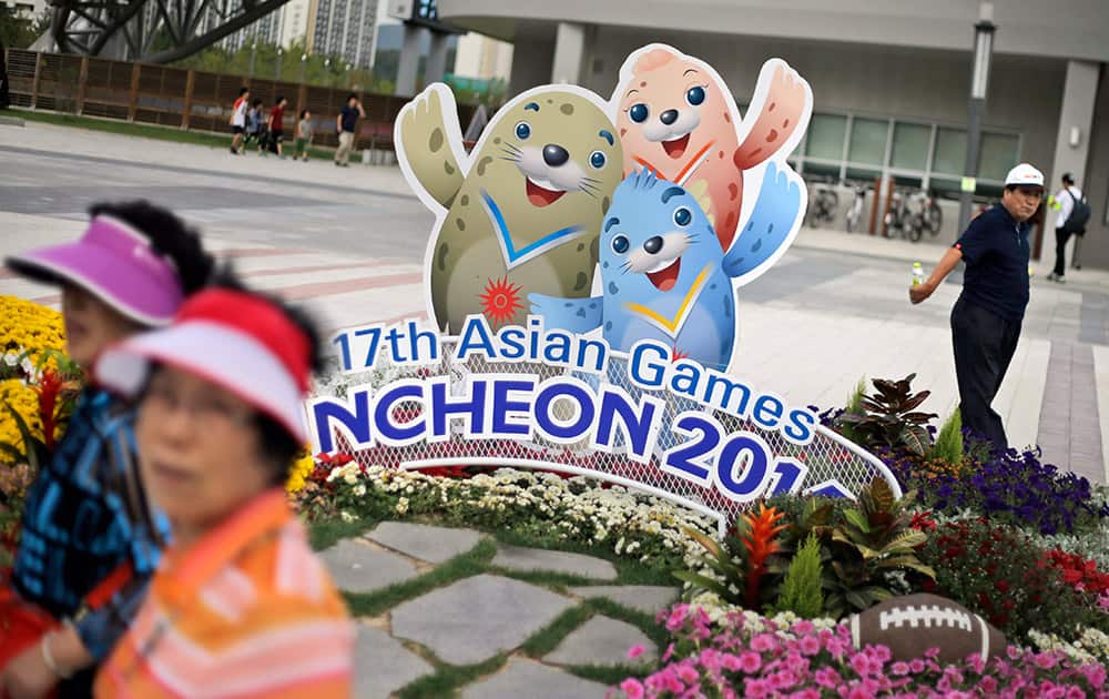 People walk past the cardboard cutouts of Barame, left, Vichuon, center, and Chumuro, the mascots of the 17th Asian Games, outside a stadium in Incheon, South Korea.