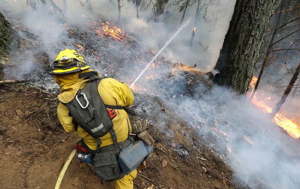 A firefighter puts water on flames approaching a containment line, while fighting the King fire near Fresh Pond, Calif.