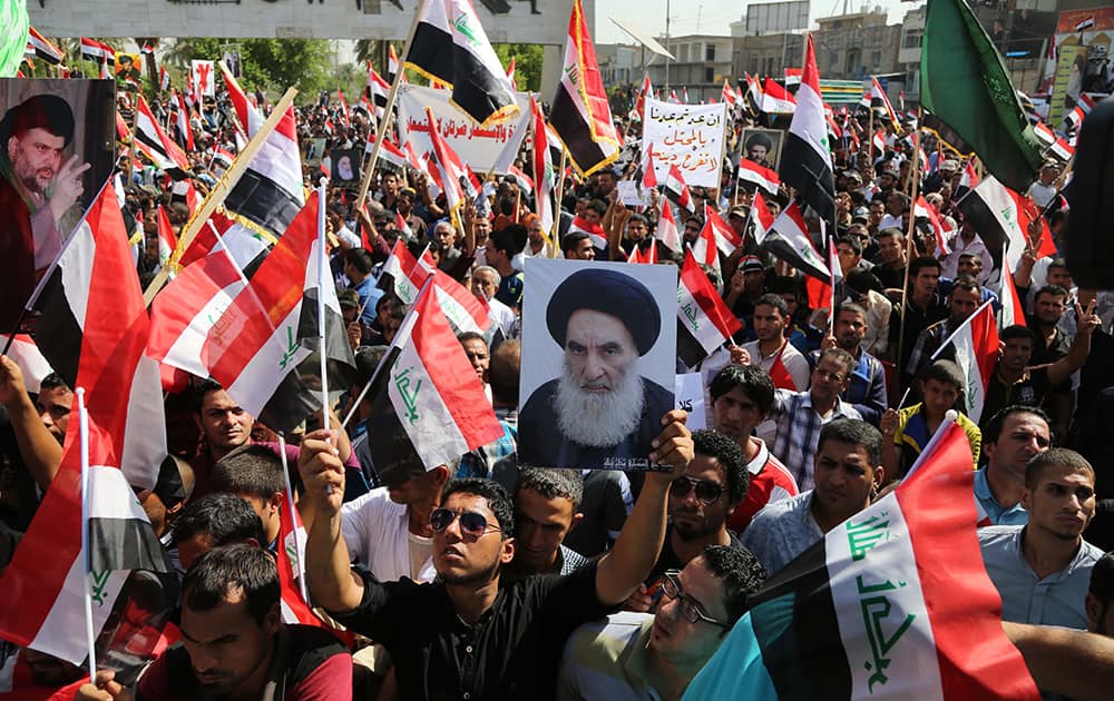 Followers of radical Shiite cleric Muqtada al-Sadr, carry a poster of Shiite spiritual leader Grand Ayatollah Ali al-Sistani, chant anti-US slogans and wave Iraqi flags during a demonstration to show their rejection to the presence of any foreign troops in Iraq, in Tahrir Square, Baghdad.