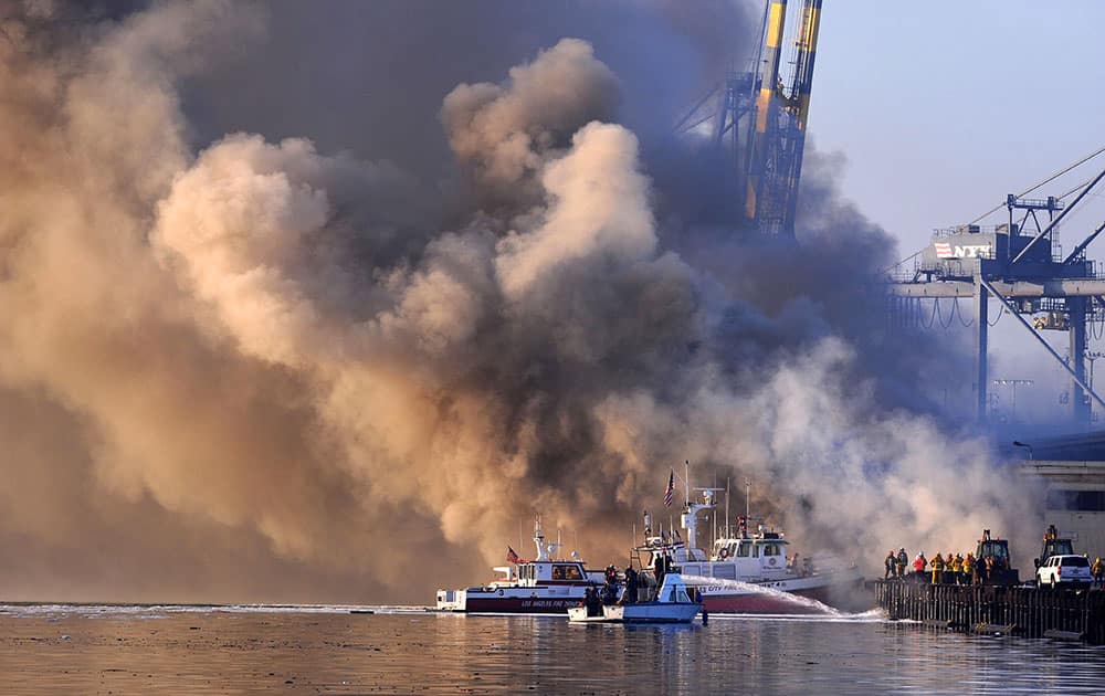 Los Angeles firefighters watch as smoke from a dock fire continues to rise as a fire boat sprays the underside of wooden pier timbers at the Port of Los Angeles in the Wilmington section of Los Angeles.