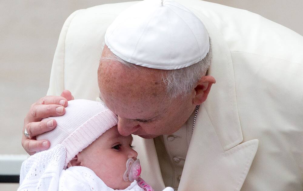 Pope Francis kisses a child as he arrives for his weekly general audience in St. Peter's Square at the Vatican.