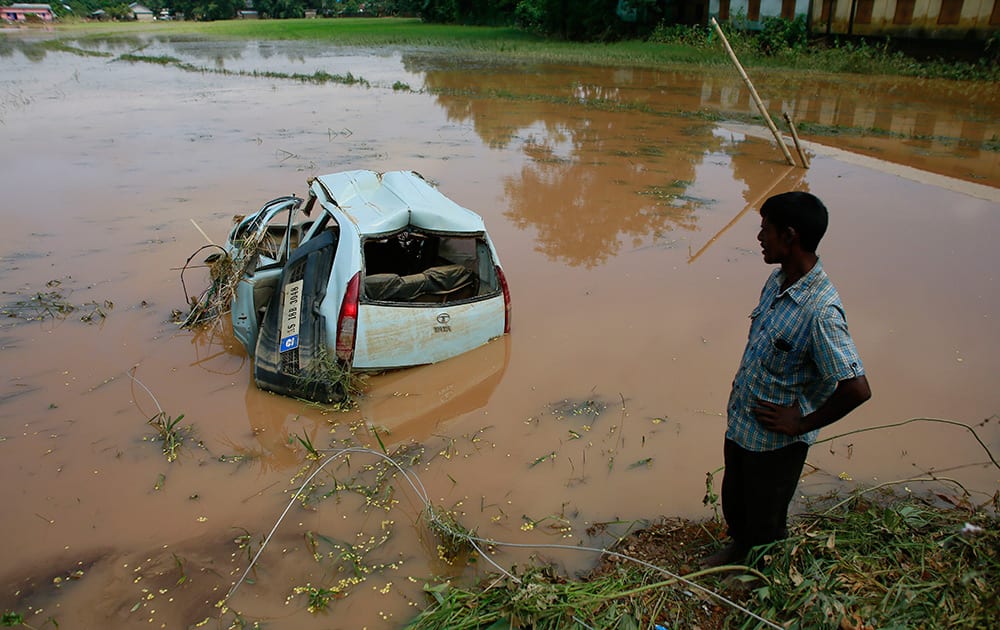 A man looks a car that got washed away in the flash floods as it lies damaged in a paddy field in Krishnai village in Goalpara district of northeastern Assam state.