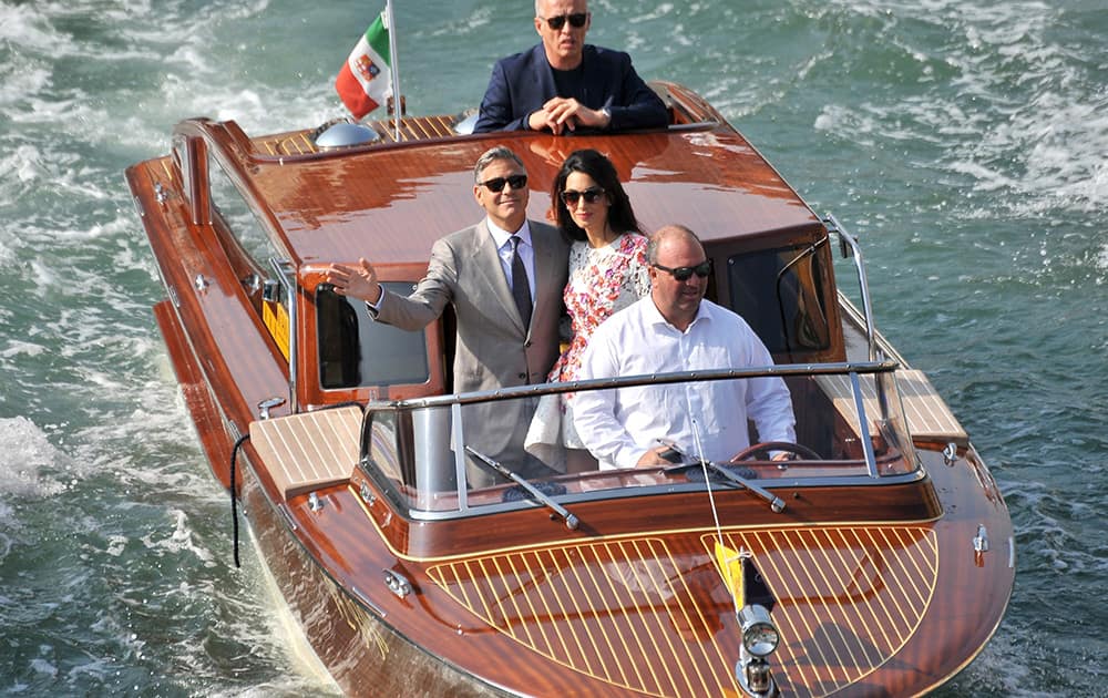 George Clooney waves as he cruises the Grand Canal on a boat with his wife Amal Alamuddin, after leaving the Aman luxury Hotel in Venice, Italy.