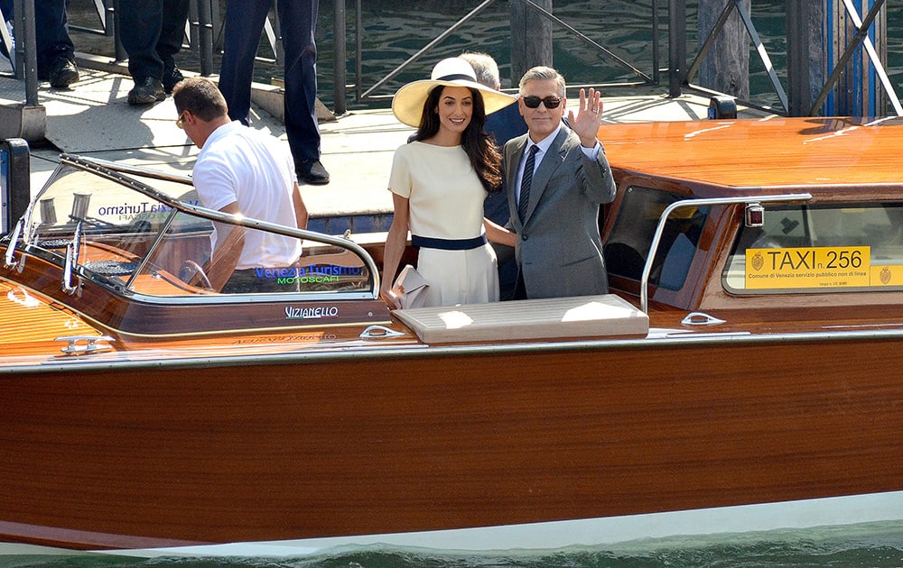 George Clooney, flanked by his wife Amal Alamuddin, waves from a water-taxi after leaving the city hall in Venice, Italy.