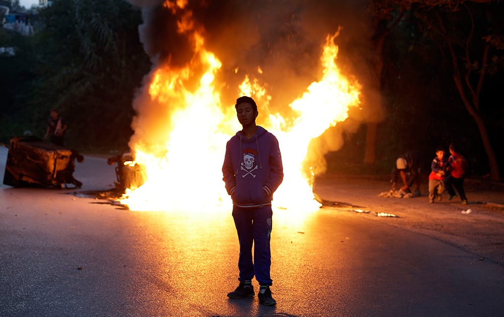 A young Roma man stands next to a burning barricade during a protest in Athens .