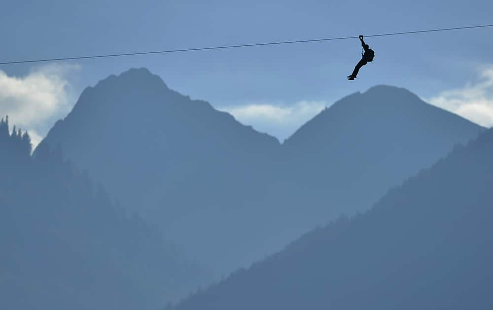 An unidentified man slips down the zip line back dropped by the mountains before the opening of the fair 'Foire du Valais' above the town of Martigny, Switzerland.