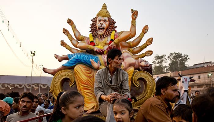 Hindu devotees sit on the top of a vehicle near an idol, signifying Hindu goddess Durga slaying the demon king Asura, as they gather at the Ramlila ground to watch the burning of effigies of demon king Ravana during Dussehra celebrations in New Delhi.