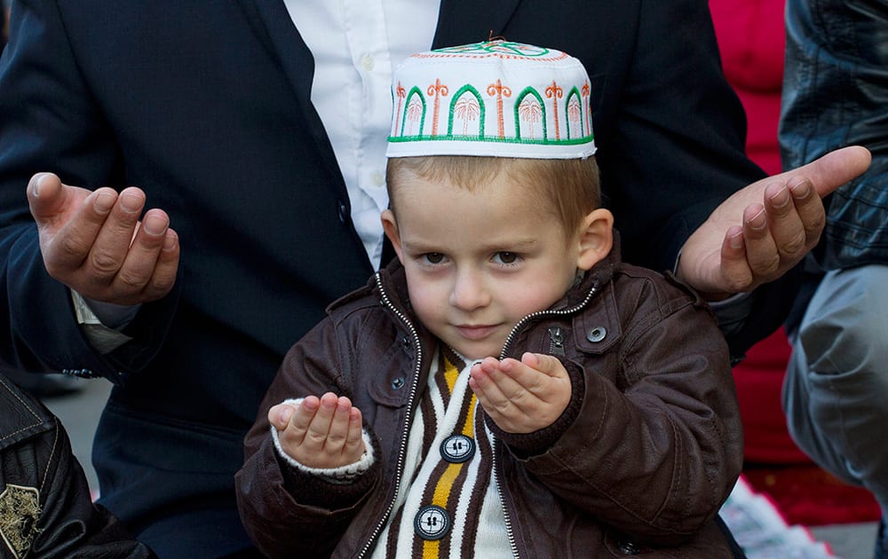 Kosovo boy sits next to his father offering Eid al-Adha prayers outside Sultan Mehmet Fatih grand mosque in the capital Pristina, Kosovo.