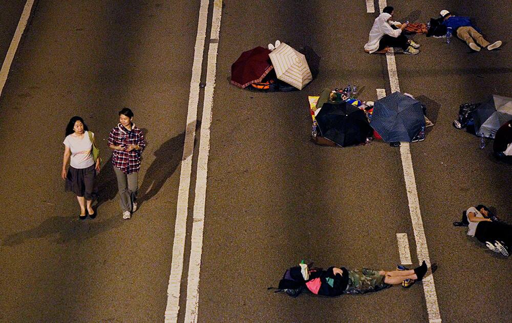 Pedestrians walk past sleeping pro-democracy student protesters on the occupied roads surrounding the government complex in Hong Kong.