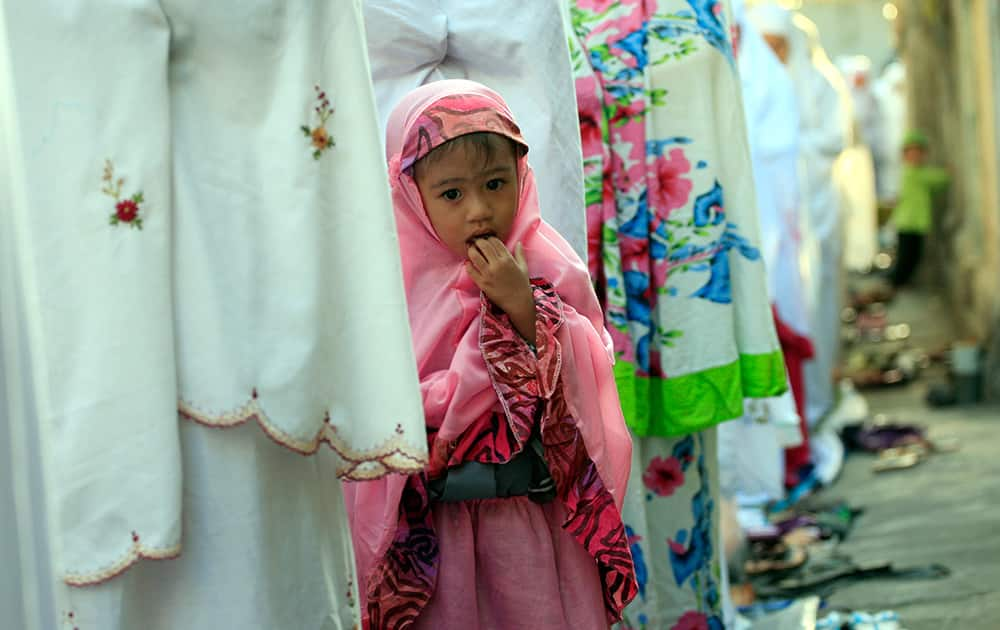 A Muslim girl stands with women offering prayers to mark the Eid al-Adha holiday on a street in Bali, Indonesia.