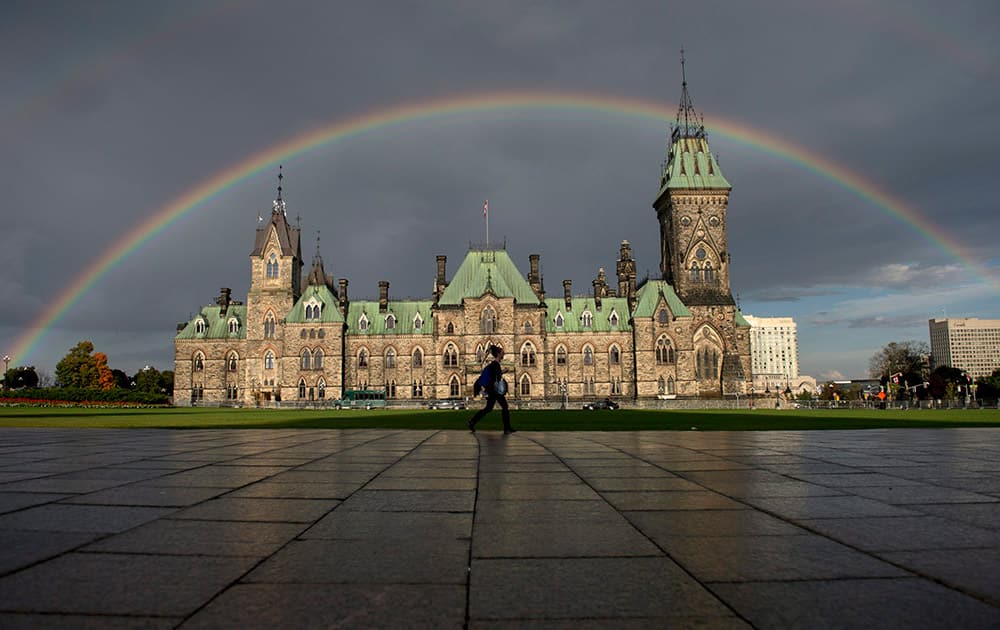 A woman walks on Parliament Hill as a rainbow arches over the East Block.