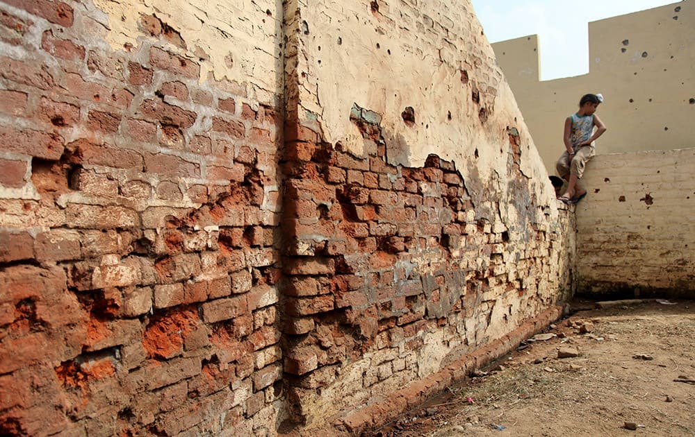 An Indian boy sits on the wall of his house with shell marks allegedly fired from the Pakistan side of the border at Flora village, in Ranbir Singh Pura, 35 kilometers (22 miles) from Jammu, India.