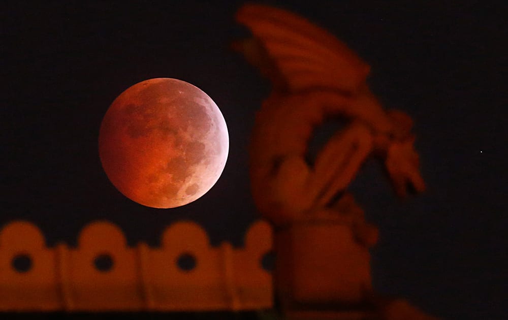 A lunar eclipse appears behind a gargoyle atop the old red Dallas County Courthouse.