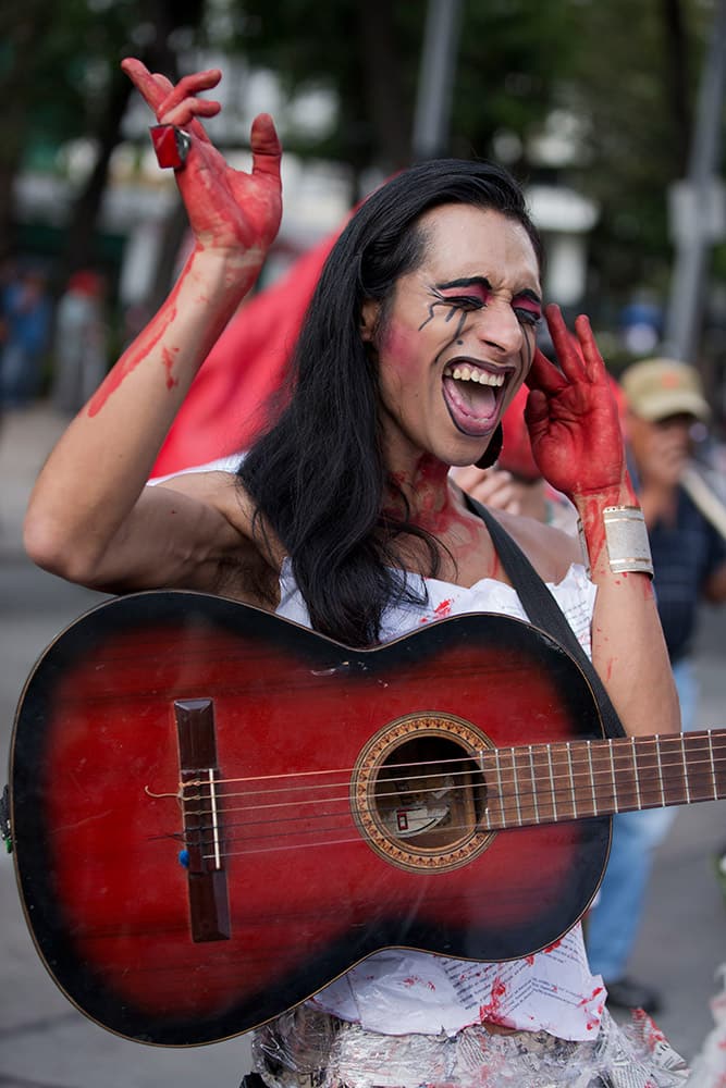 A man with fake blood on his hands and wearing a dress of crumpled paper sings anti-government songs as thousands marched through the capital to demand that the government find the 43 students who disappeared in southern Guerrero State, in Mexico City.