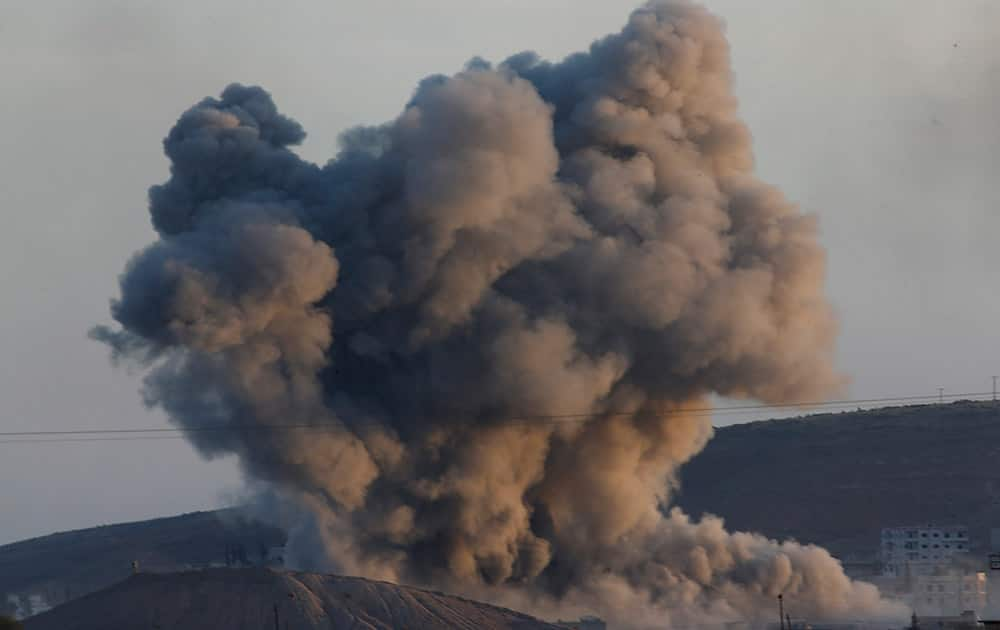 a huge plume of smoke rises after an airstrike in eastern Kobani, Syria, behind a hilltop where militants with the Islamic State group had raised their flag on Monday, as fighting intensified between Syrian Kurds and the militants as seen from Mursitpinar on the outskirts of Suruc, at the Turkey-Syria border. 