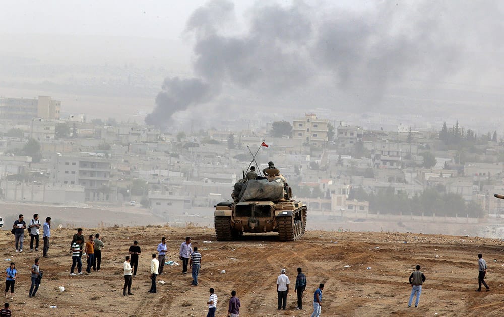 Civilians gather to watch fighting between Syrian Kurds and the militants of Islamic State group alongside Turkish soldiers aboard a tank holding a position overlooking the town Kobani, Syria, on a hilltop on the outskirts of Suruc, at the Turkey-Syria border.