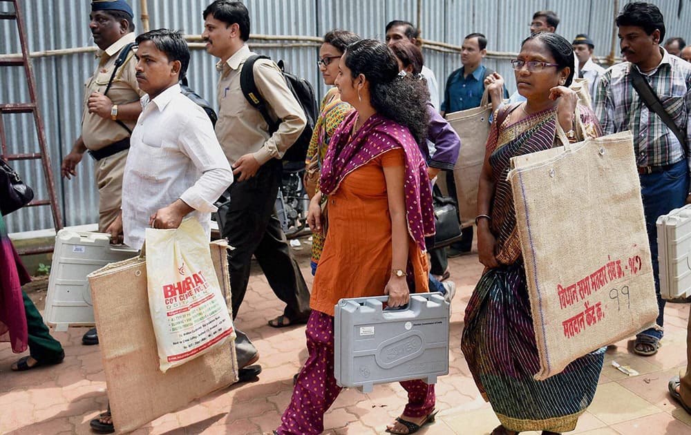 Election officials carry EVMs as they leave for polling stations from a distribution centre on the eve of voting for Assembly elections, in Mumbai.