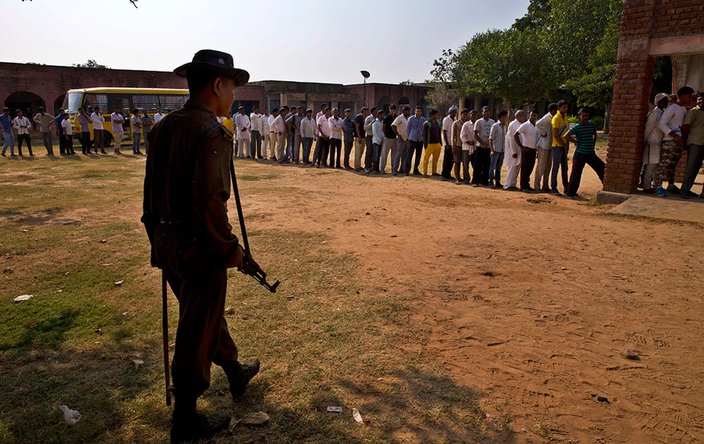 A security man guards as voters line up to cast their votes during the Haryana state elections in Bandhwadi.